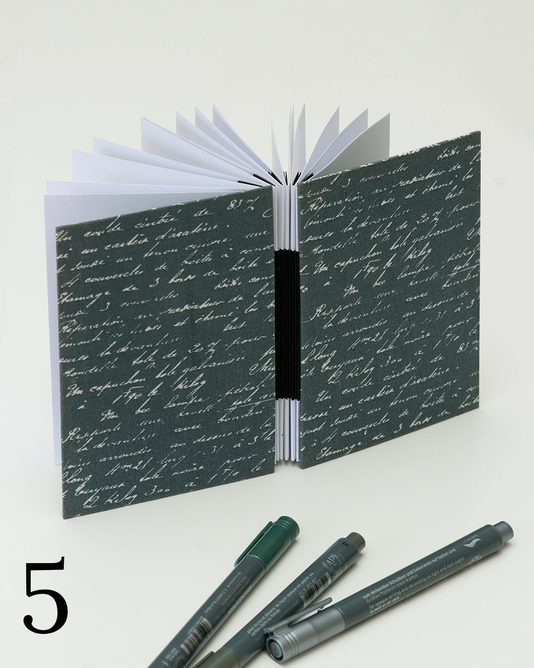 Quaderno per hand lettering con rilegatura australiana, copertina in tessuto grigio con testo manoscritto bianco, dorso a fisarmonica nero
