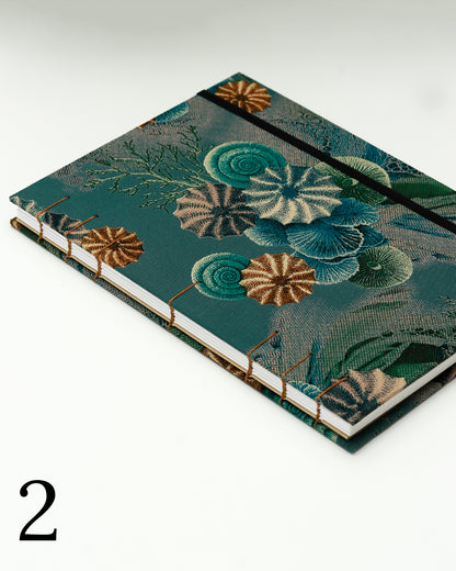 Quaderno per calligrafia con rilegatura copta, copertina in tessuto stampato con conchiglie e ricci di mare stile tavola naturalistica ottocentesca su fondo verde petrolio, elastico e filo golden brown