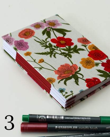 Quaderno per hand lettering con rilegatura australiana, copertina in tessuto floreale rosa, rosso e viola su fondo bianco, dorso a fisarmonica rosso