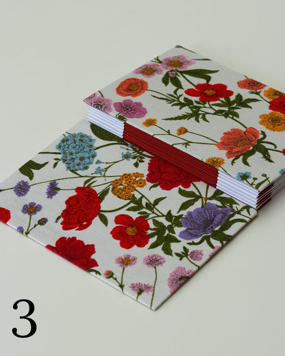 Quaderno per hand lettering con rilegatura australiana, copertina in tessuto floreale rosa, rosso e viola su fondo bianco, dorso a fisarmonica rosso