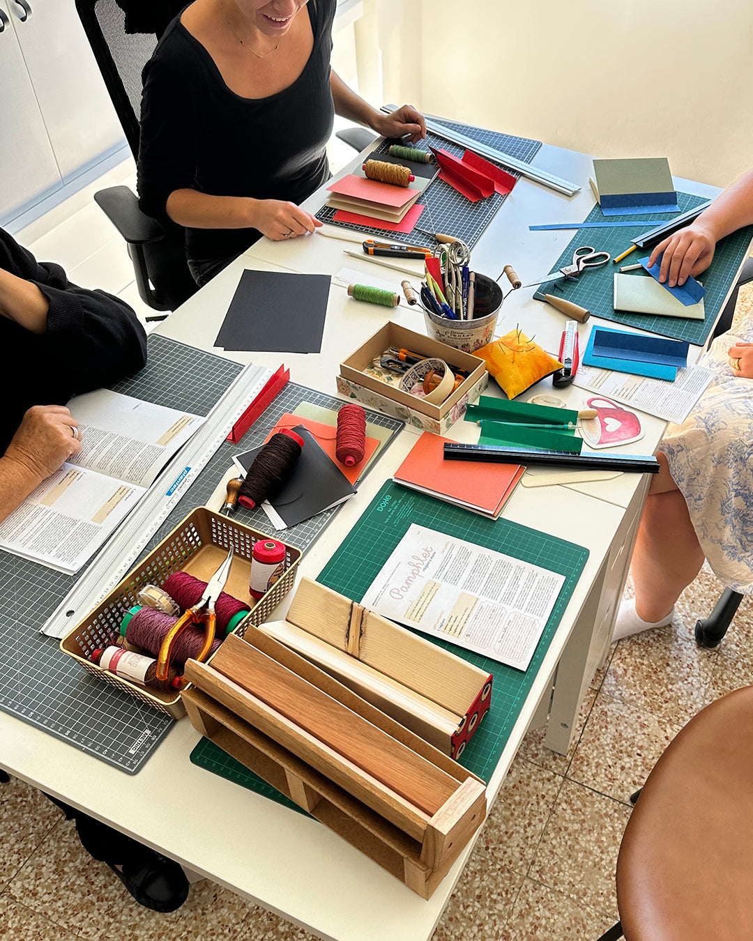 tavolo e persone durante un laboratorio creativo di rilegature con fili e carte