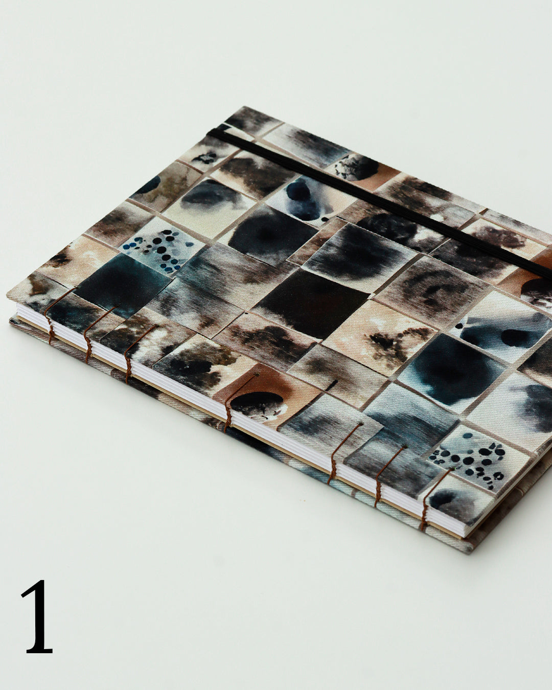 Quaderno per calligrafia con rilegatura copta, copertina in tessuto a griglia patchwork con macchie d'inchiostro blu, nero, marrone e crema, elastico nero, filo marrone