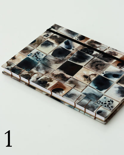 Quaderno per calligrafia con rilegatura copta, copertina in tessuto a griglia patchwork con macchie d'inchiostro blu, nero, marrone e crema, elastico nero, filo marrone