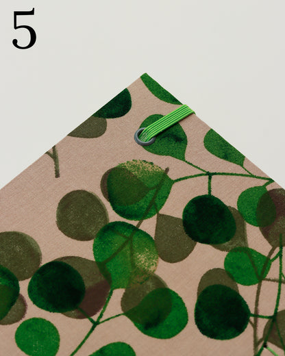 Quaderno per calligrafia con rilegatura copta, copertina in tessuto con foglie di eucalipto verdi su fondo tortora chiaro, elastico e filo verde, occhielli grigi