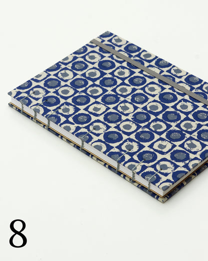 Quaderno per calligrafia con rilegatura copta, copertina in tessuto a motivo geometrico con cerchi concentrici blu navy e crema, elastico e filo grigio