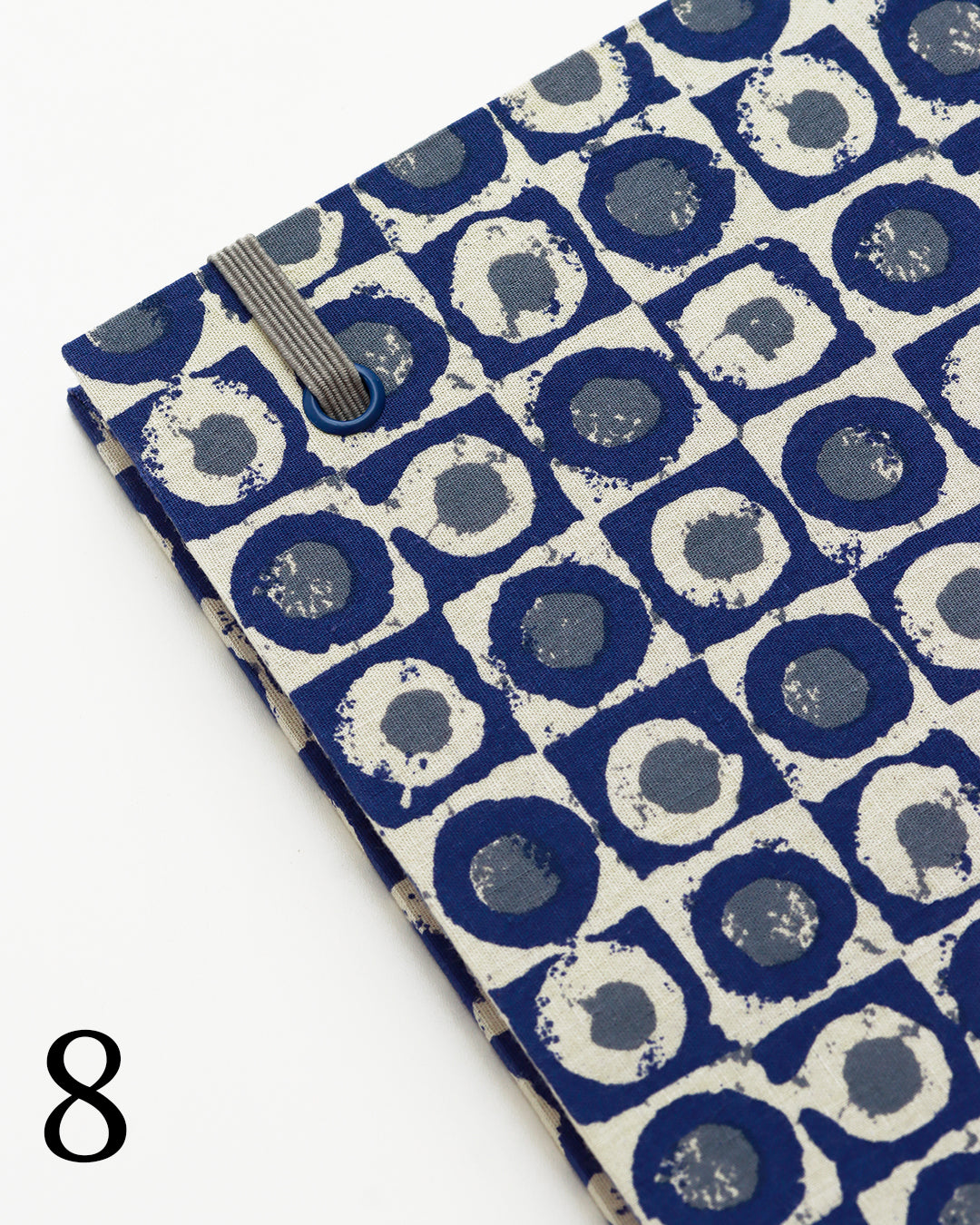 Quaderno per calligrafia con rilegatura copta, copertina in tessuto a motivo geometrico con cerchi concentrici blu navy e crema, elastico e filo grigio