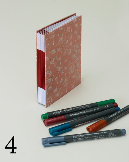 Quaderno per hand lettering con rilegatura australiana, copertina in carta di lokta color terracotta con motivo di semi di tarassaco, dorso a fisarmonica rosso