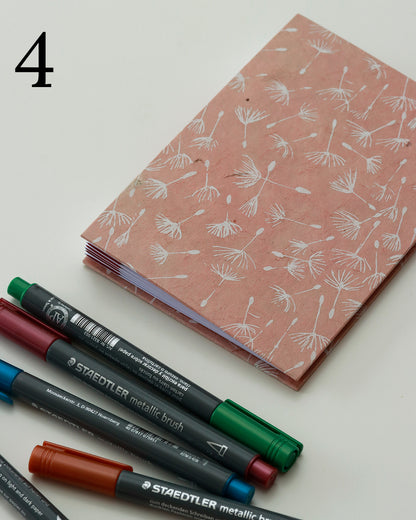 Quaderno per hand lettering con rilegatura australiana, copertina in carta di lokta color terracotta con motivo di semi di tarassaco, dorso a fisarmonica rosso