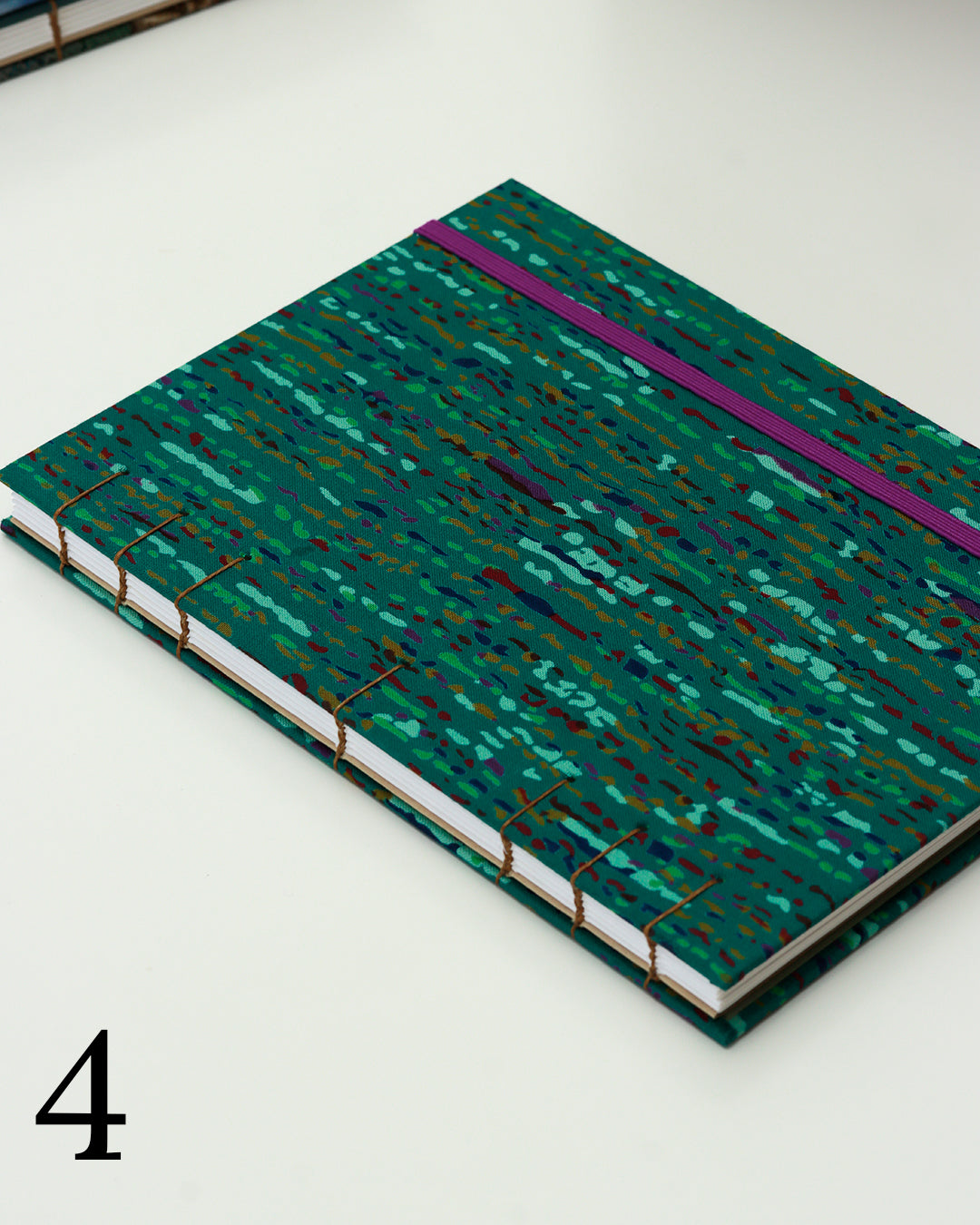 Quaderno per calligrafia con rilegatura copta, copertina in tessuto verde smeraldo con trattini e macchioline multicolore, elastico viola, occhielli blu, filo golden brown