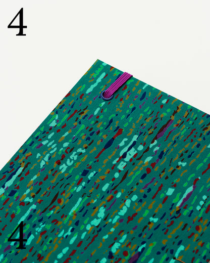 Quaderno per calligrafia con rilegatura copta, copertina in tessuto verde smeraldo con trattini e macchioline multicolore, elastico viola, occhielli blu, filo golden brown