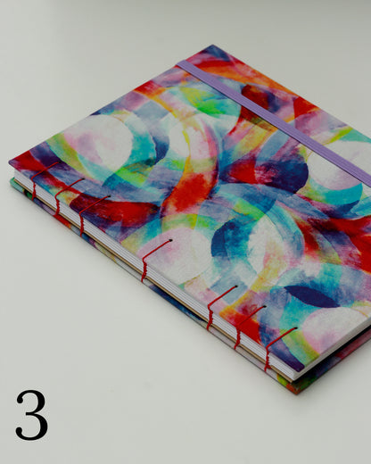 Quaderno per calligrafia con rilegatura copta, copertina in tessuto con cerchi e forme sovrapposte in acquerello multicolore, elastico lilla, filo rosso