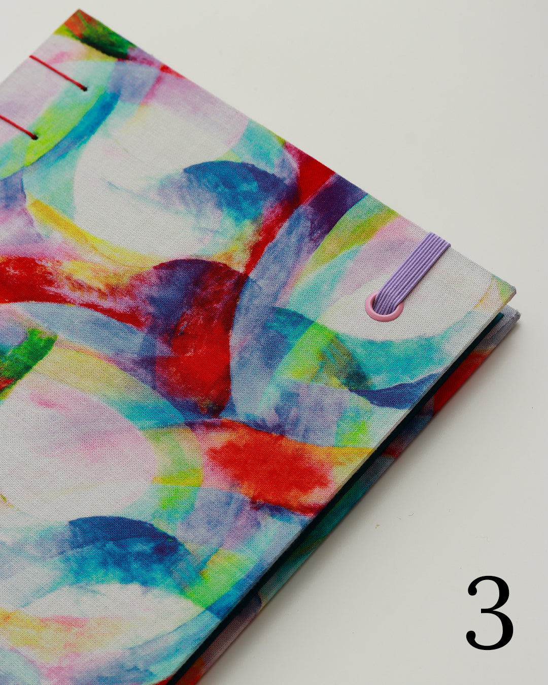 Quaderno per calligrafia con rilegatura copta, copertina in tessuto con cerchi e forme sovrapposte in acquerello multicolore, elastico lilla, filo rosso
